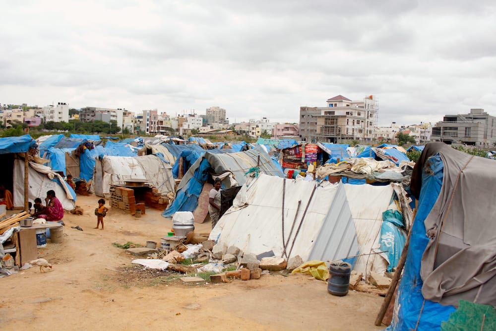  Many tarp covered structures in the foreground, larger buildings in the background.